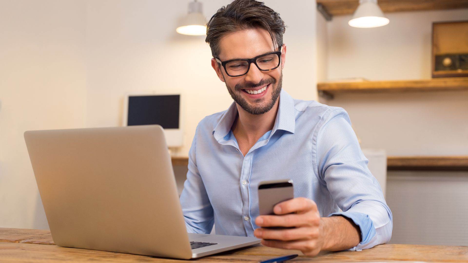 Man Smiling While Using Smartphone And Laptop